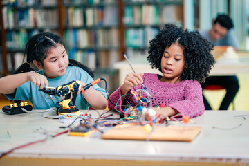 Two children intense following robotics assembly success, using robot kits, electronics, creative problem solving, STEM collaboration, inspiring education moment inside quiet library classroom.