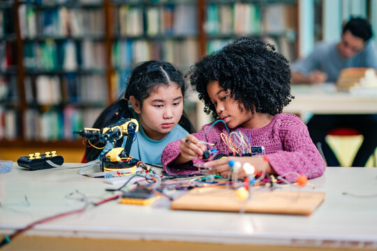 Two students helping in robotics project works successfully, surrounded by wires, robot tools, hands on STEM education, teamwork achievement, joyful learning experience in academic environment.