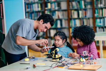 Fototapeta premium Teacher leads robotics activity by showing proper wiring technique, guiding students through electronic project, STEM skill development, focused learning environment inside modern library space.