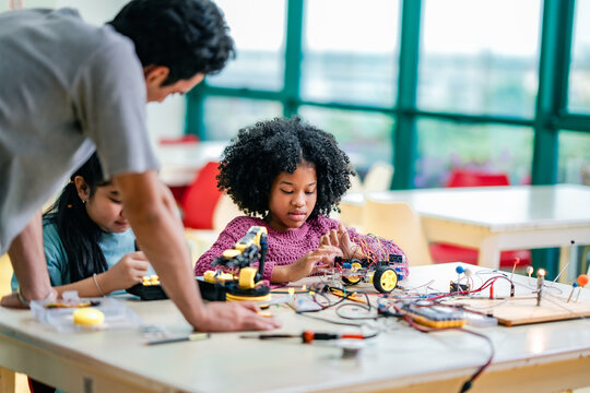 Caucasian teacher demonstrates robotics assembly for African American girl, Asian girl, supporting STEM knowledge growth, diversity education values, hands on technology learning. - Powered by Adobe