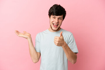 Young Russian man isolated on pink background holding copyspace imaginary on the palm to insert an ad and with thumbs up