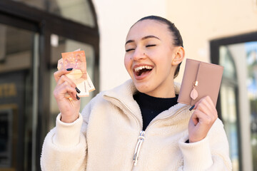 Young moroccan girl  at outdoors holding wallet with money with happy expression
