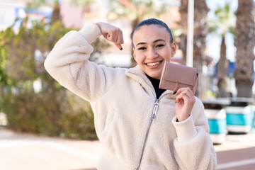 Young moroccan girl  at outdoors holding a wallet and celebrating a victory