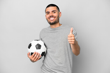 Young football player man isolated on grey background with soccer ball and with thumb up
