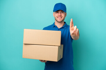 Delivery caucasian man isolated on blue background with fingers crossing and wishing the best