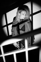 A stylish woman in a coat stands on the stairs. Black and white noir style.