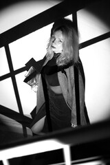 A stylish woman in a coat stands on the stairs. Black and white noir style.