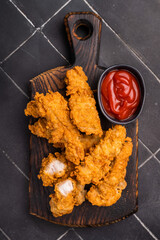 Fried chicken tenders or strips with hot sauce. black background. top view © Mironov