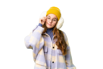 Teenager girl wearing winter muffs over isolated chroma key background with glasses and happy