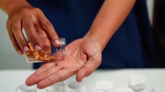 A man is pouring small yellow health capsule from the bottle into an open palm