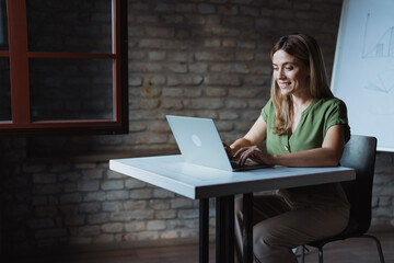Focused businesswoman sitting at her desk, using a laptop and managing her startup business independently