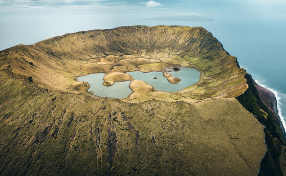 Aerial view of the unique caldera on the top of Corvo Island during sunny day with the crater lakes and meadows inside the caldera surrounded by the turquoise waters of Atlantic Ocean, Azores Islands