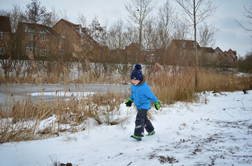 Child running near reed in residential area with snow. Winter kids activity.