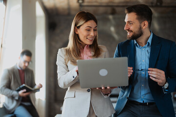 Two business professionals discussing project while looking at laptop in modern office