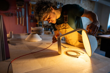 Handcrafted lamp made from personal blueprints. Artisan man contemplating wire choice, doubts in creative process, refining design to perfection, examining connection point, plug in connect
