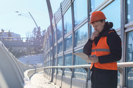 Pensive builder reviewing notes on winter overpass with glass barrier
