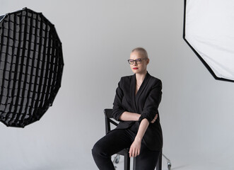 Confident Woman in Professional Attire Sitting in Photography Studio. Female cancer survivor. Smiling Woman with Glasses Posing Confidently in a Studio Environment. Model Has Glaucoma