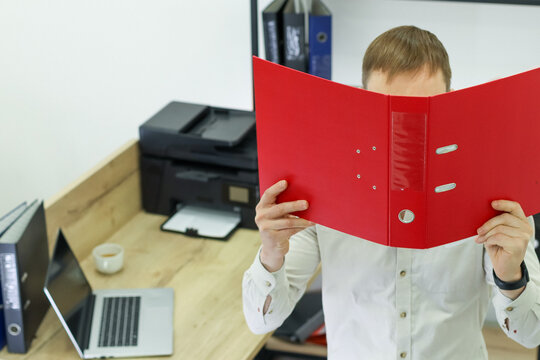 Worker hiding behind red folder at office desk