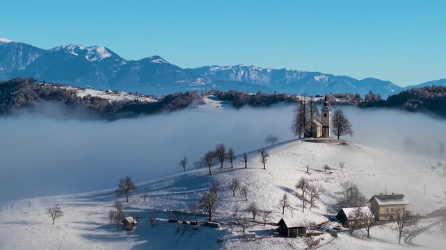 Breathtaking Winter Mountain Range in Fog: Epic Aerial view of Jamnik church in the clouds , morning light. 4k hd 60 fps drone footage. Slovenian Alps