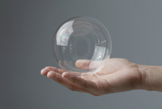 Hand holding a clear, floating glass sphere against gray.