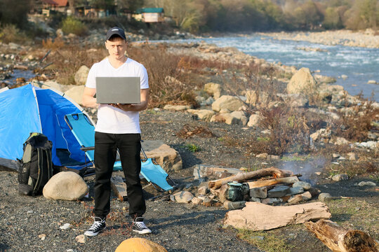 Man with laptop at riverside camp in cap