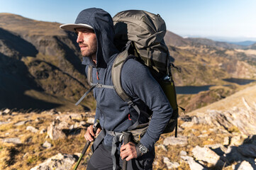 Focused hiker climbing rocky ridge with trekking poles