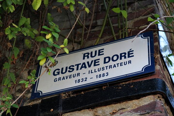 Rue Gustave Dor&eacute;. Graveur - Illustrateur. 1832 - 1883. Plaque de nom de rue sur un mur de briques rouges avec plantes grimpantes.