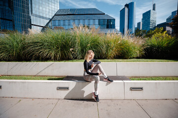 Woman in athletic wear sitting on a bench in a modern city park with skyscrapers