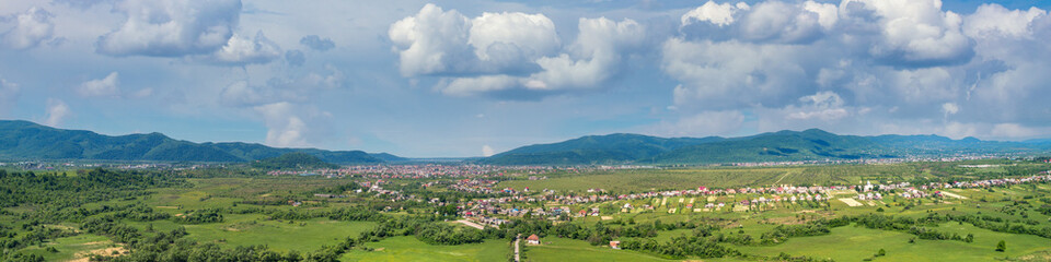 Obraz premium Panoramic view of mountains valley. Green field and trees in spring on a sunny day. View from above
