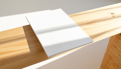 Blank white canvas on a wooden surface with sunlight casting shadows