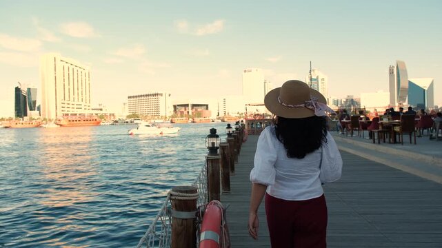 woman walking on deck bridge at Al seef Dubai with heritage Emirati architecture and old Dubai skyline, 4k pro res travel video