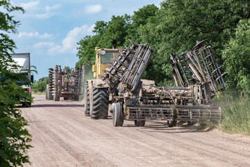 Agricultural machinery convoy driving on rural dirt road. Heavy tractors with cultivators returning from field work, modern farming, soil cultivation, agriculture industry, summer countryside.
