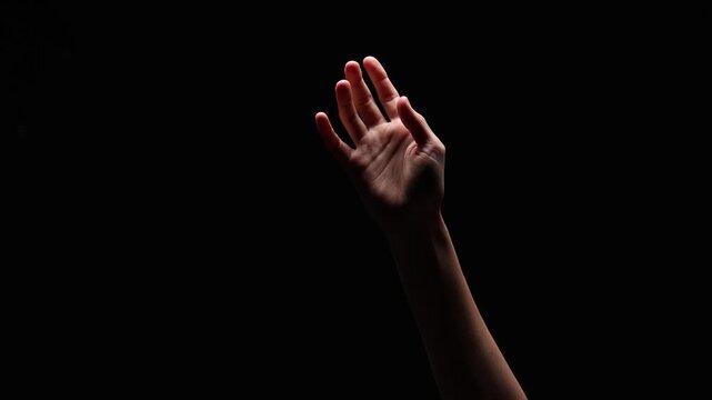 A single open hand is raised and illuminated against a black background, conveying emotion and openness. Ample copy space