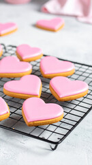 Several heart shaped cookies with pink icing are arranged neatly on a cooling rack in a kitchen.