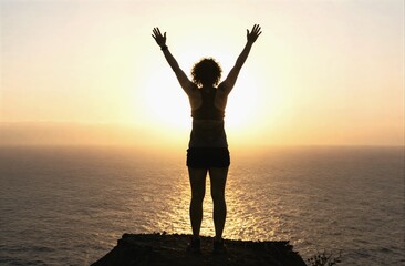 Fototapeta premium Woman standing on cliff raising arms at sunset