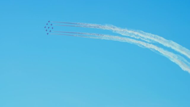 Nine red jets performing synchronized aerial maneuver leaving white smoke trails against clear blue sky