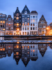 Iconic Amsterdam canals and traditional Dutch architecture at twilight with warm city lights reflecting in the water. Picturesque evening view of Amsterdam historical district at dusk.