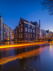 Beautiful Amsterdam canal at twilight with historic dutch architecture and city lights reflected in the water. Picturesque evening view of Amsterdam historical district at dusk.