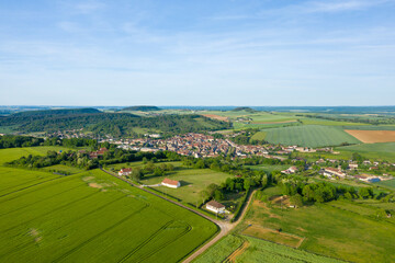 Fototapeta premium Aerial view of Varzy village nestled among lush green farmland and gentle hills, with geometric field patterns and scattered rural houses beneath a clear blue sky.