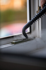 Cleaning the window. A man with steam device removes dirt from the plastic window frame.