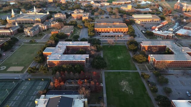 Multi court tennis complex with fenced green courts sits beside red brick dorms and academic halls, bordered by lawns, trees, and warm late day sunlight near the I 35 corridor in Waco, Texas