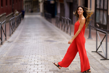 A Young Woman Dressed in a Striking Red Jumpsuit Strolling Through a Charming City Street