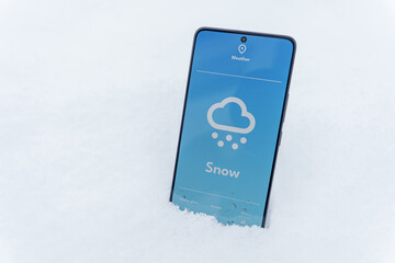 Smartphone lying in snow with snow forecast on weather app screen, winter outdoors concept
