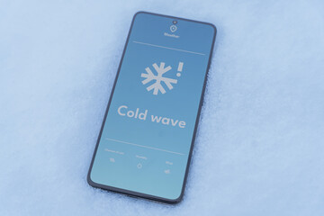 Smartphone lying in snow with cold wave alert on weather app screen, winter outdoors concept