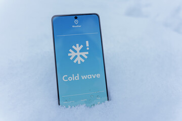 Smartphone lying in snow with cold wave alert on weather app screen, winter outdoors concept