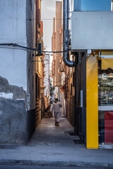 Man Walking Through Narrow Alley Between Buildings in Urban Street Scene at Dusk, Quiet, Agadir, Morocco