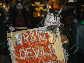 Villach, Austria - December 01, 2023: Krampuslauf festival features a horned figure holding a sign reading "Red Devils," showcasing traditional winter celebrations and festive atmosphere