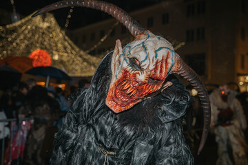 Villach, Austria - December 01, 2023: Krampuslauf festival scene featuring a horned creature in a dark costume, surrounded by festive lights and a lively crowd, celebrating winter traditions