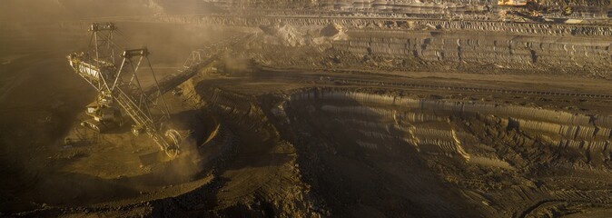High resolution panoramic view of massive mining machines in an open pit coal mine, surrounded by dust. Powerful industrial scene showing large scale extraction, energy production, and human impact.