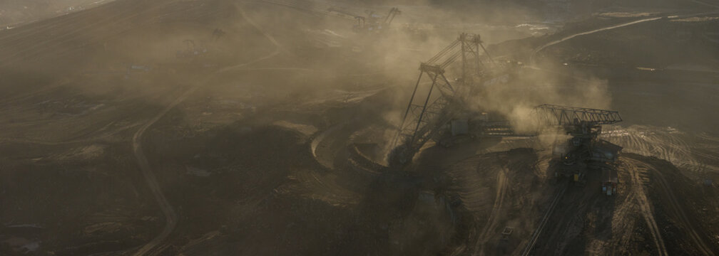 High resolution panoramic view of massive mining machines in an open pit coal mine, surrounded by dust. Powerful industrial scene showing large scale extraction, energy production, and human impact.